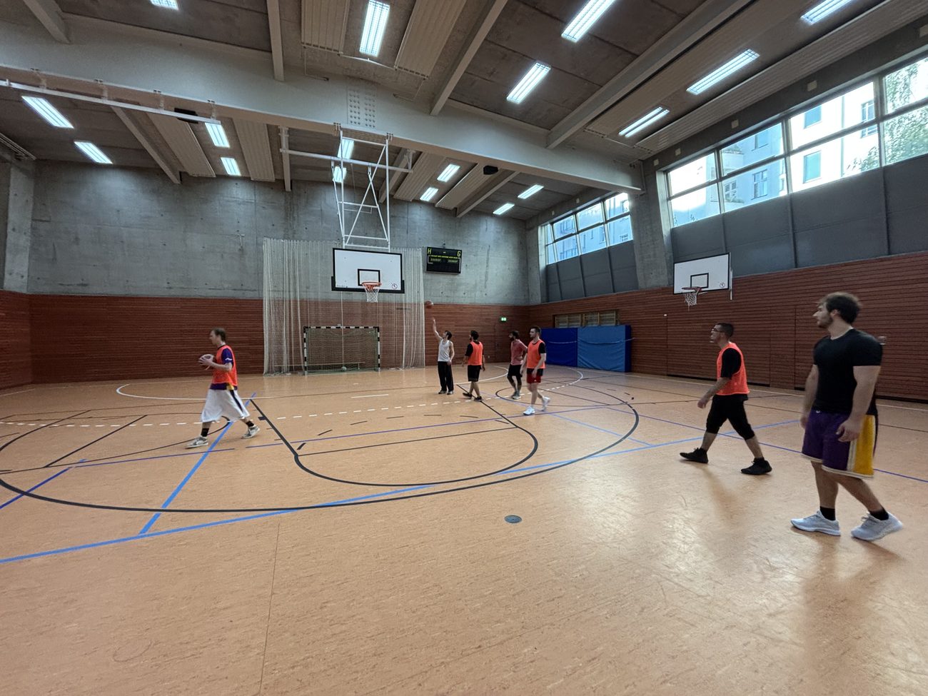 Training in der Halle: mehrere Spieler in Leibchen verteilt über das Feld, im Hintergrund der Korb.